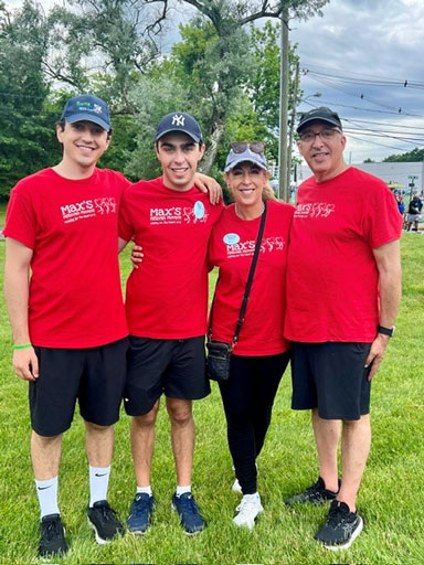 Group of four wearing red shirts posing together outdoors on a grassy field, smiling; two young men, a woman, and an older man.