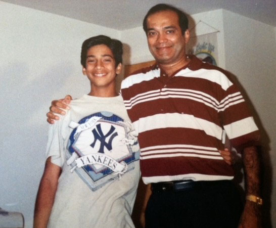 Rajesh-Karnani-and-Sham-Karnani-for-web | NJ Sharing Network Two people pose indoors: a smiling boy in a New York Yankees T‑shirt standing beside an older man in a red‑and‑white striped polo shirt, arms around each other.