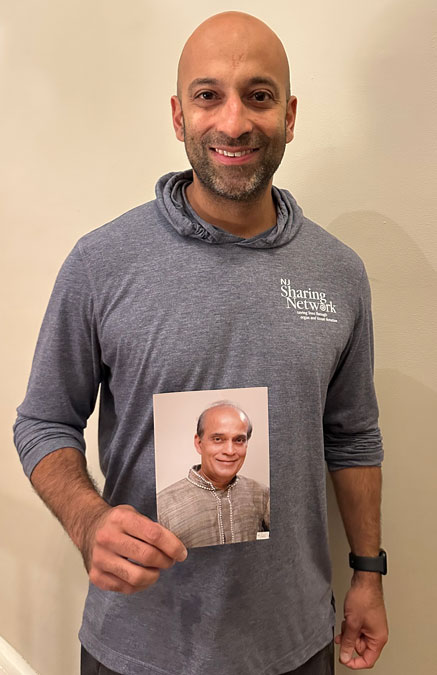 Rajesh-Karnani-for-web | NJ Sharing Network Bald man wearing a gray Sharing Network hoodie holds a photo of himself in front of a beige wall.