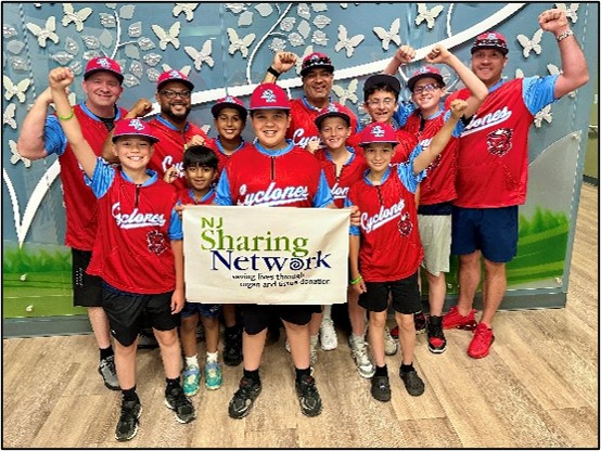 Group of kids and coaches in red Cyclones jerseys pose indoors, holding a banner that reads NJ Sharing Network.