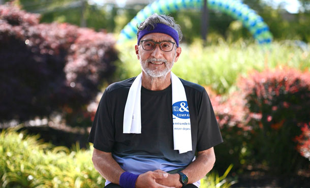 Chris-Carrales-2 | NJ Sharing Network Older man with a gray beard and purple headband sits outdoors, smiling, with towels draped around his neck.