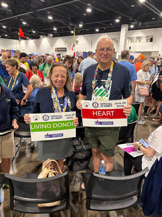 Rich-and-Donna-Albanese-DeMair-2 | NJ Sharing Network Two smiling donors pose at a crowded event, holding signs reading 'LIVING DONOR' and 'HEART' with 'Official Attempt' and date June 20, 2026.