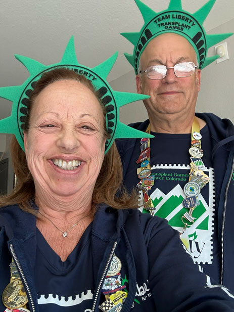 Rich-and-Donna-Albanese-DeMair-3 | NJ Sharing Network Two smiling adults wearing green Statue of Liberty hats with pins, posing for a selfie at the Transplant Games.