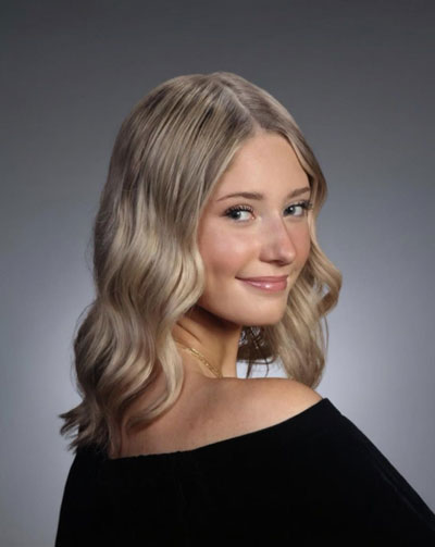 Victoria-Pribish | NJ Sharing Network Portrait of a smiling woman with shoulder-length blonde, wavy hair against a gray studio backdrop, wearing a black top.