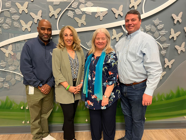 Four adults posing and smiling for a photo in front of a butterfly wall display.