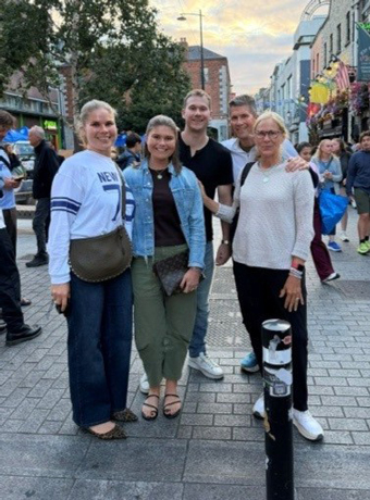 5---Matt-Felix-and-Family---Wife-Trish-and-kids-Andrew-Katie-Caroline | NJ Sharing Network Cinco amigos posan para una foto en una concurrida calle de la ciudad, sonriendo con las tiendas y los peatones de fondo.