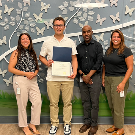 Alexander-Rausch_presentation | NJ Sharing Network Four adults pose in front of a butterfly mural; the person second from the left holds a blue-folder certificate.