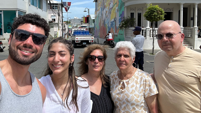 Tony-Moyet-and-family | NJ Sharing Network Cinco adultos posan para hacerse un selfi en una calle soleada, con un mural de colores y un camión aparcado al fondo.