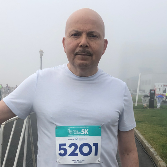Tony-Moyet-at-NJ-Sharing-Network-5K | NJ Sharing Network Hombre con camiseta blanca posando en un hipódromo envuelto en niebla, con el dorsal número 5201 para una carrera de 5 km.