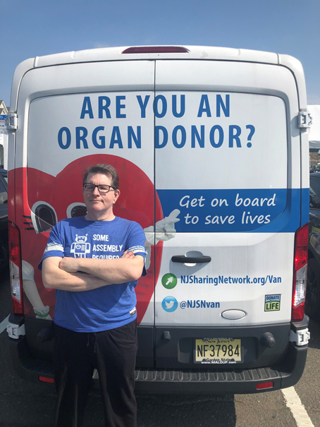 James-Condon---Liver-Transplant-Recipient | NJ Sharing Network White van rear displaying 'Are you an organ donor?' banner; man in blue shirt stands with arms crossed beside a red heart graphic.